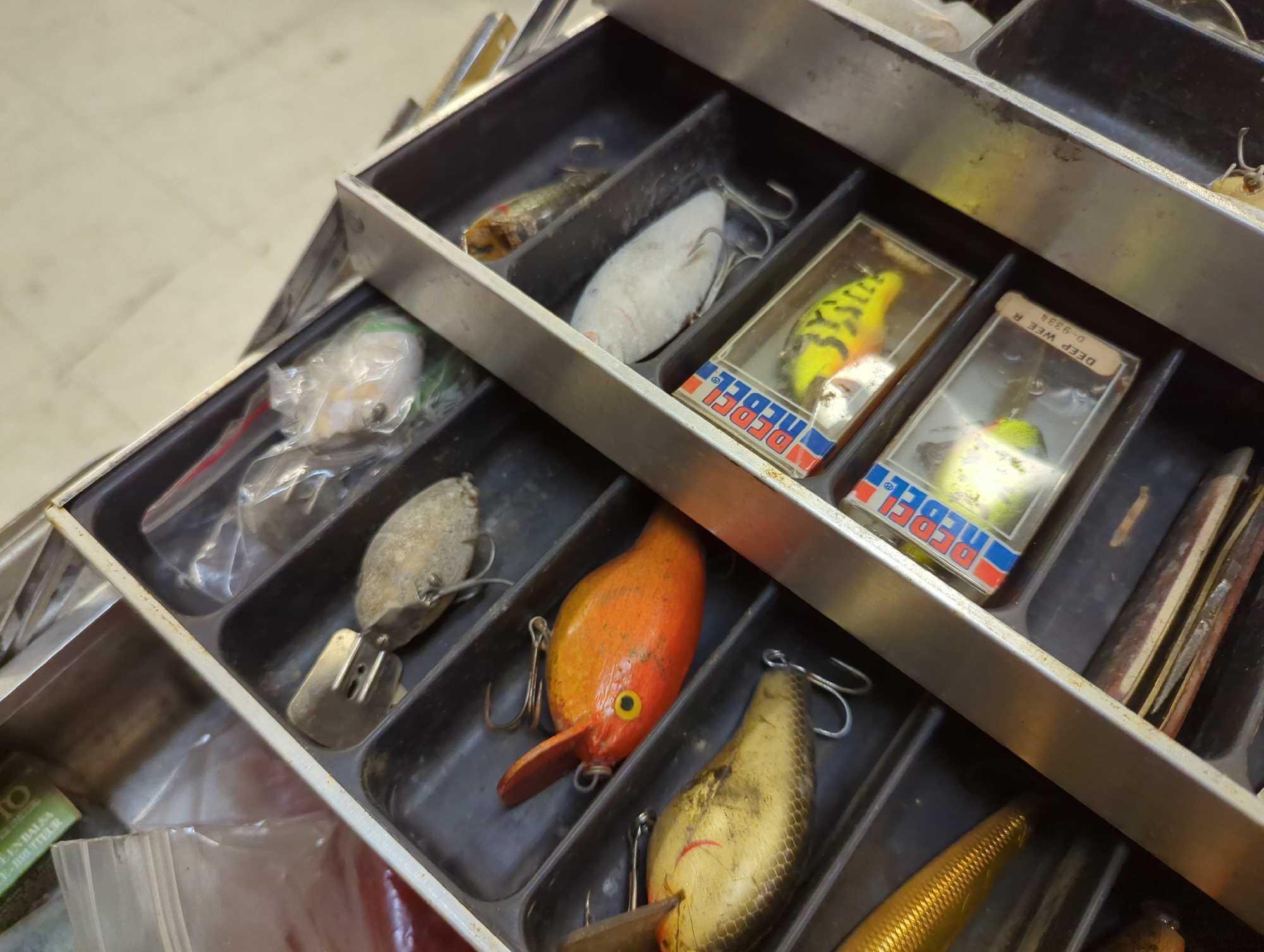 Large metal tackle box and contents including various fishing lures and other fishing accessories.